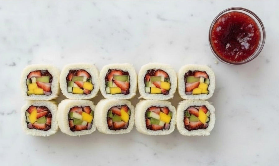 Sliced dessert sushi rolls filled with fruit and a bit of Mrs. Ruth's Special Reserve Raspberry Jam arranged on a white marble board, with a small jar of raspberry jam alongside, garnished with fresh raspberries and mint leaves