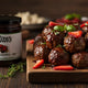 Mrs. Ruth's Balsamic Strawberry Slow Cooker Meatballs stacked on a cutting board with a jar of jam sitting beside it.