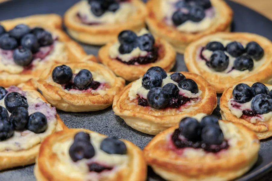 Mini blueberry lemon basil tarts with cream cheese filling, fresh blueberries, and a drizzle of Mrs. Ruth's Blueberry Lemon Basil Preserves